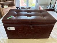 Rectangular dark brown vinyl ottoman with tufted lid and embossed floral front panel