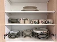 Three-shelf cabinet showing stacked plates, bowls, mugs, sugar bowl and platters