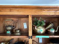 Shelf showing three brass kettles and small brass stand