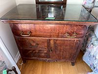 Frontal view of washstand showing drawers, door, brass pulls, and glass top
