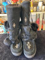 Front view of black Manitobah Mukluks showing beadwork, fur and pom-poms