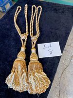Pair of matching braided curtain tiebacks with tassels displayed on dark surface