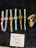 All seven watches laid flat on black surface showing fronts and straps