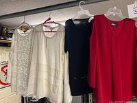 Front view of four tops hanging: ivory lace, ivory knit with lace hem, black knit, red blouse
