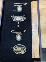 Overall view of four brooches beside ruler for scale