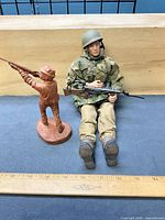 GI Joe figure seated next to carved wood soldier, scale shown