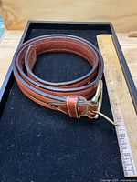 Full view of coiled brown leather belt beside ruler