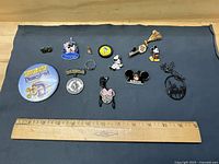 Overview of all Disney pins, earrings, necklaces, ring and button laid out with ruler for scale.