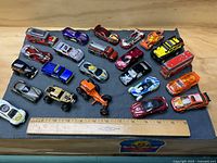 Overall view of 19 die-cast vehicles on cloth with ruler for scale