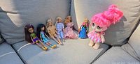 Seven dolls lined on sofa: two Monster High, three Barbies, Anna, Kindi Kids