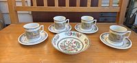 Set of four mugs with saucers and one bowl displayed on tabletop