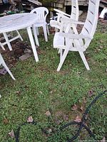 White plastic oval patio table, two chair styles visible, grass setting