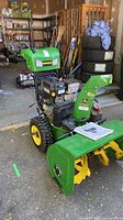 Full view of John Deere 1028E snow blower showing auger, chute, wheels and manual on housing
