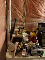 Table with airbrush compressor, roller covers, spray cans, hand tools