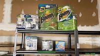 Two Bounty paper towel multipacks, Lysol cleaner box, Frank garbage bags box, OxiClean box on shelving