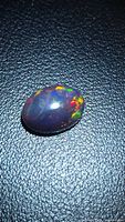 Top view of oval black opal showing multicolour play of colour