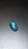Oval black opal on textured surface showing green flash