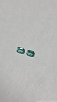Pair of cushion-cut emeralds on neutral background