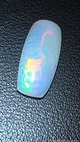 Elongated cushion Ethiopian opal on textured black surface showing green flash