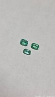 Three cushion-cut emeralds on neutral background