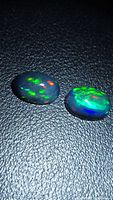 Two black opal cabochons on black background displaying multicolour flash