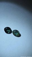Two oval green-blue sapphires on light background