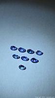 Eight oval bluish-violet gemstones on neutral background