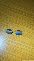 Two oval cabochon stones on wood surface, chatoyancy visible
