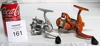 Silver and orange spinning reels beside can for scale