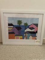 Front view of framed artwork showing colorful coastal village scene, white mat and frame