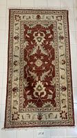 Front view of the hand-knotted wool rug showing burgundy field, cream border and fringe