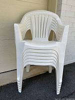 Stack of six white plastic patio armchairs showing style, color and condition