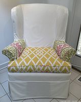 Front view of wing chair showing white slipcover, yellow geometric seat cushion, patterned armrests