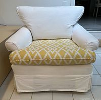 Front view of white slipcovered armchair showing yellow geometric seat cushion and white back cushion