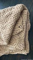 Folded beige crochet blanket showing overall texture and scalloped edge