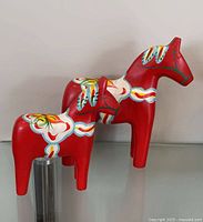 Two red hand-painted wooden Dala horses on glass shelf