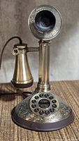 Full view of brass-tone candlestick telephone with ornate base and rotary-style dial