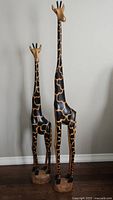 Front view of both wooden giraffe statues displaying height difference and painted pattern