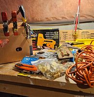 Overview of lot showing stapler box, clamps, extension cord and hardware on workbench