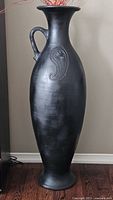 Full view tall black pottery vase standing on floor
