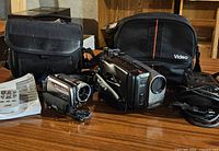 Both camcorders, both cases, charger, manual and cable on table