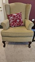 Front view of upholstered wingback chair showing fabric color, leg style, and accent pillow