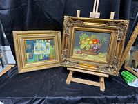 Two framed artworks on easel and table
