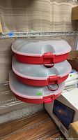Three red plastic wreath storage cases stacked on shelf