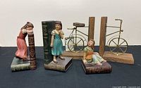 Overview of four bookends: two resin girl figurines on faux books, two wood/brass bicycle bookends