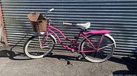 Full view of pink cruiser bicycle against corrugated metal wall