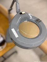 Close view of Luxo magnifier head showing lens, grey housing, switch