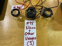 Three magnifiers on table with lot tag showing two Nikon square-body loupes and one cylindrical loupe