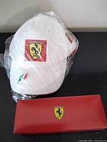 White Ferrari cap in plastic next to red Ferrari box