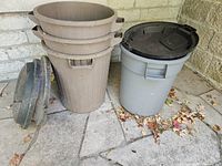 Stack of three brown ribbed plastic garbage cans, grey garbage can with lid, two separate lids